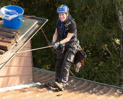 Höhenarbeiterin begeht Steildach per Seilzugangstechnik